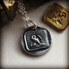 A Mother's Love Wax Seal Necklace next to another medallion over a white background.